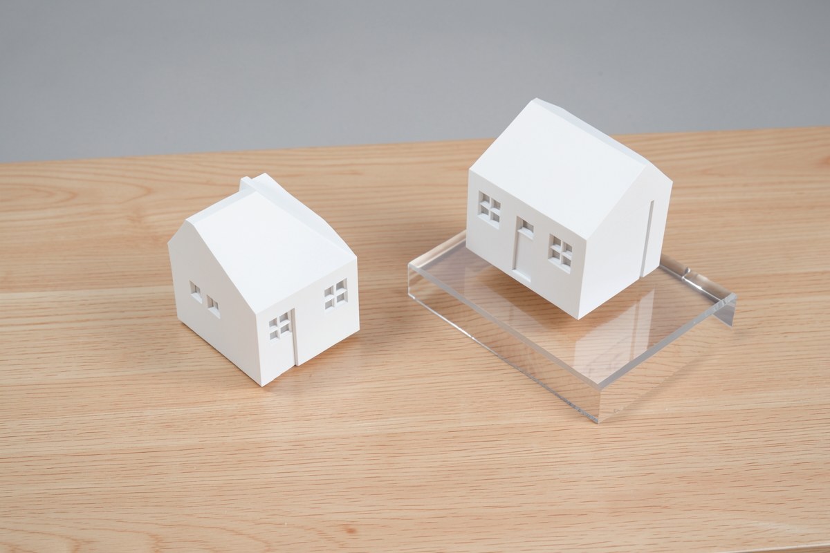 Two identical model houses on a table, one slightly elevated, representing a side-by-side comparison of mortgage options.